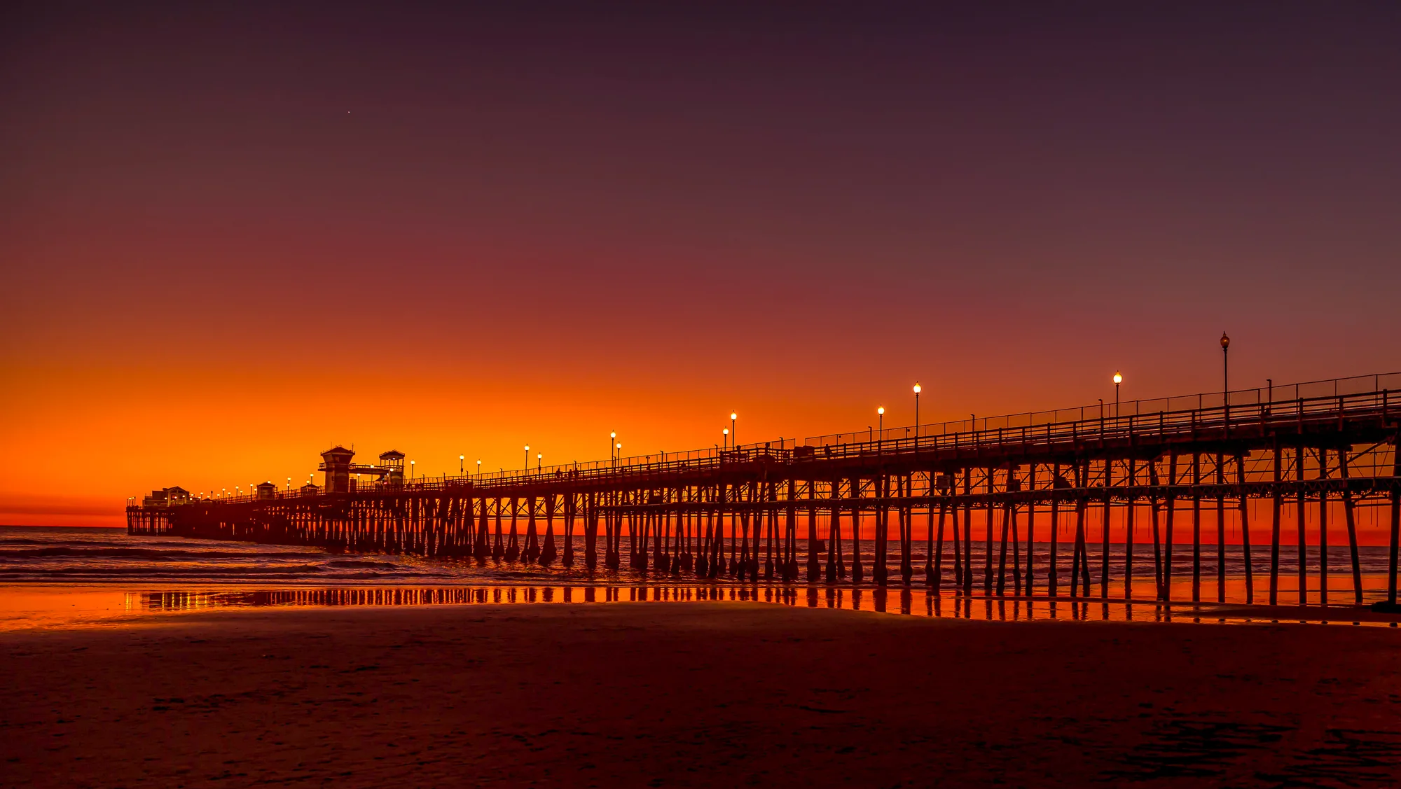 Ocean pier silhouetted against glowing sunset horizon