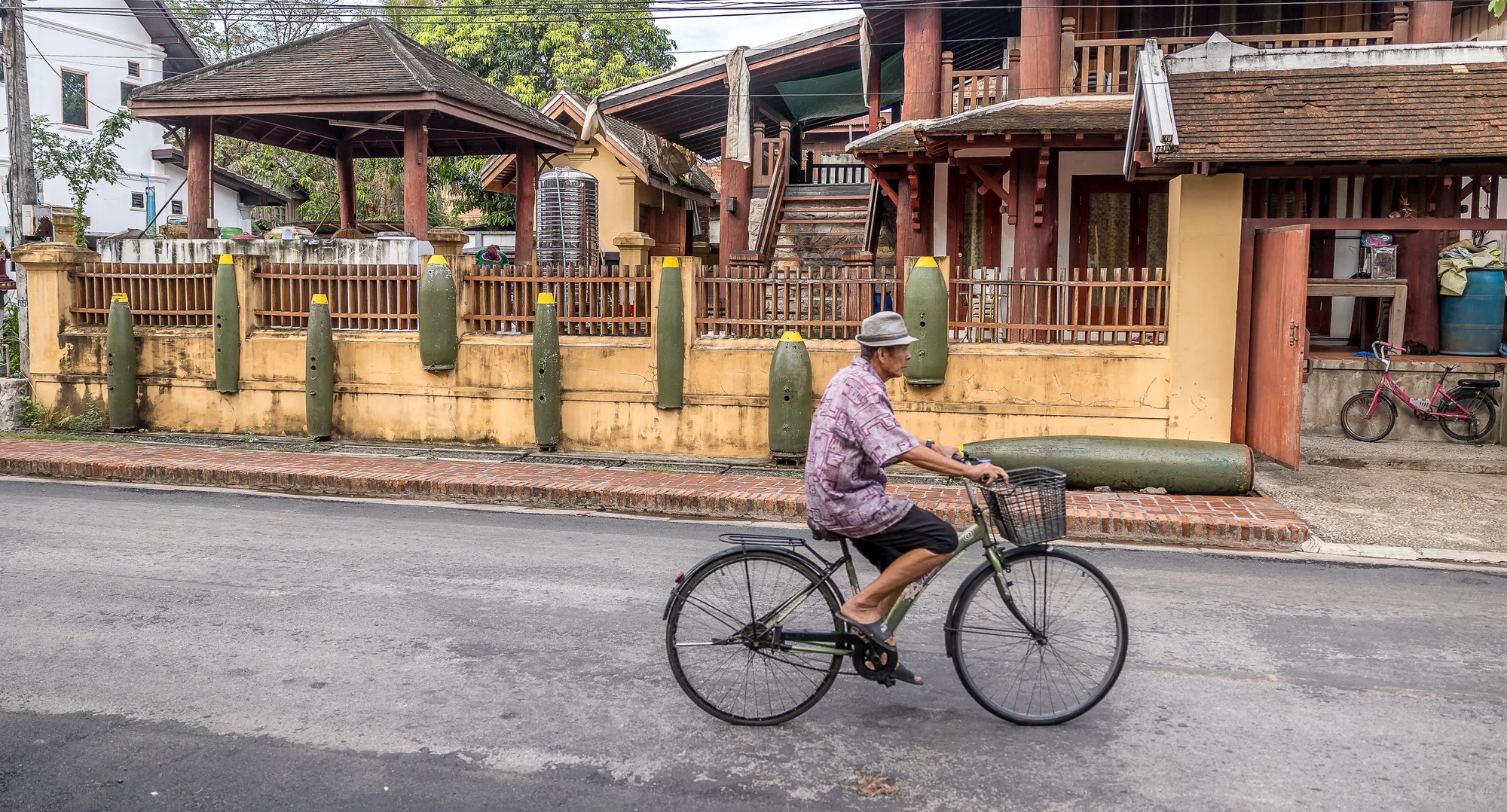 Cyclist traveling past historic bomb casings in rural Laos